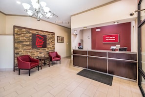 A Red Roof Inn reception area with a stone wall, two red chairs, a reception desk, and a sign indicating free Wi-Fi in all rooms. - Red Roof Inn Clarksville (Clarksville)