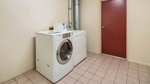 A laundry room with a front-loading washer and dryer, a metal exhaust vent, and a red door. - Red Roof Inn Clarksville (Clarksville)