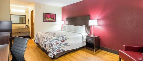 Una habitación de hotel con cama, escritorio, silla, mesita de noche y lámpara.