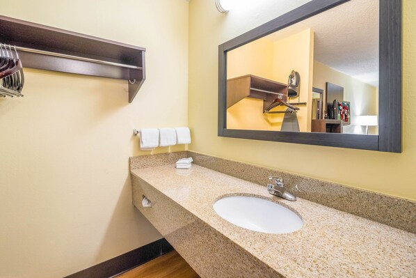 A bathroom with a granite countertop, a white sink, a towel rack with towels, and a mirror reflecting a towel rack and a heater. - Red Roof Inn Clarksville (Clarksville)