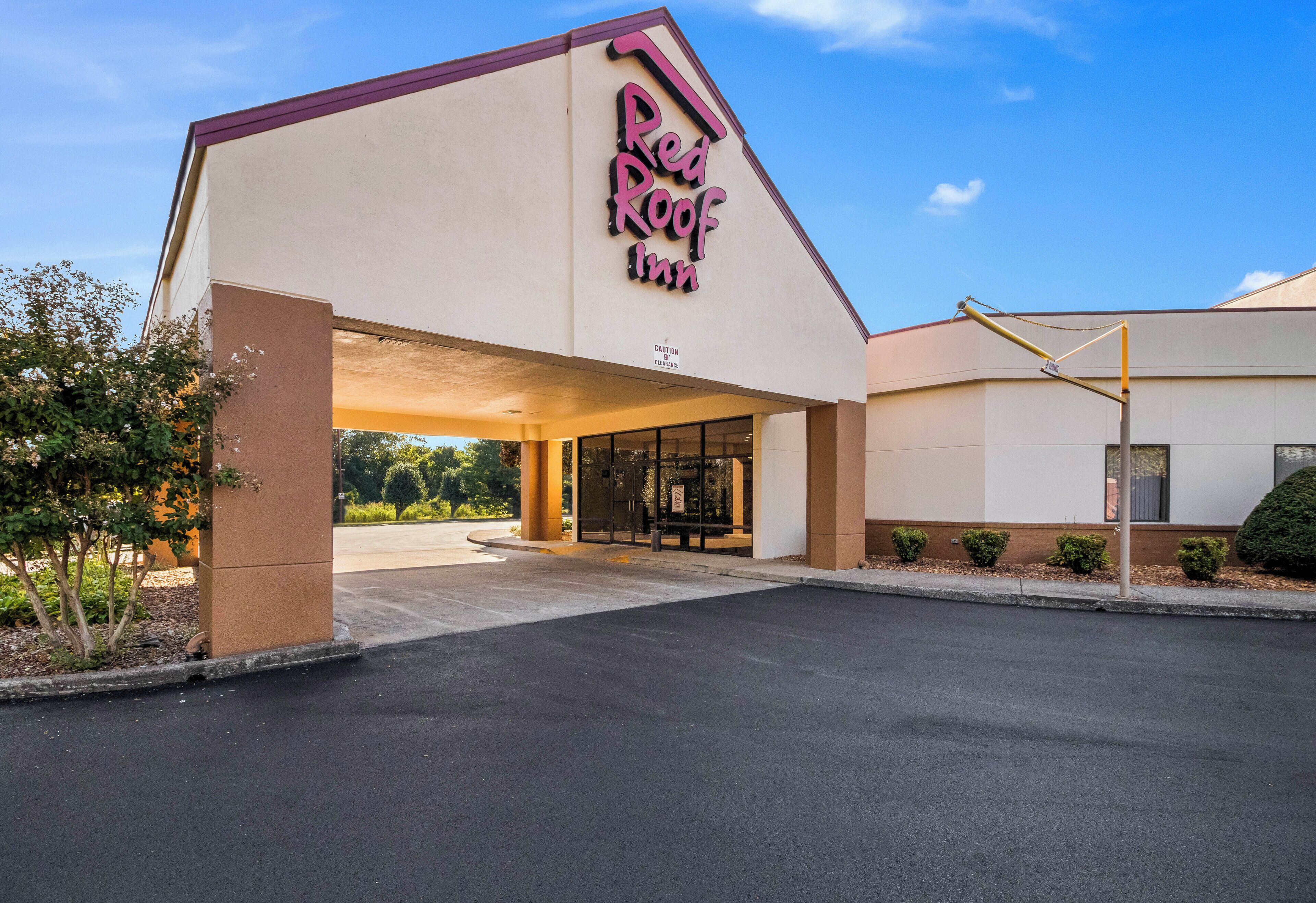 L’entrée d’un hôtel, avec un ciel dégagé, une enseigne indiquant « Red Roof Inn » et un espace de stationnement.