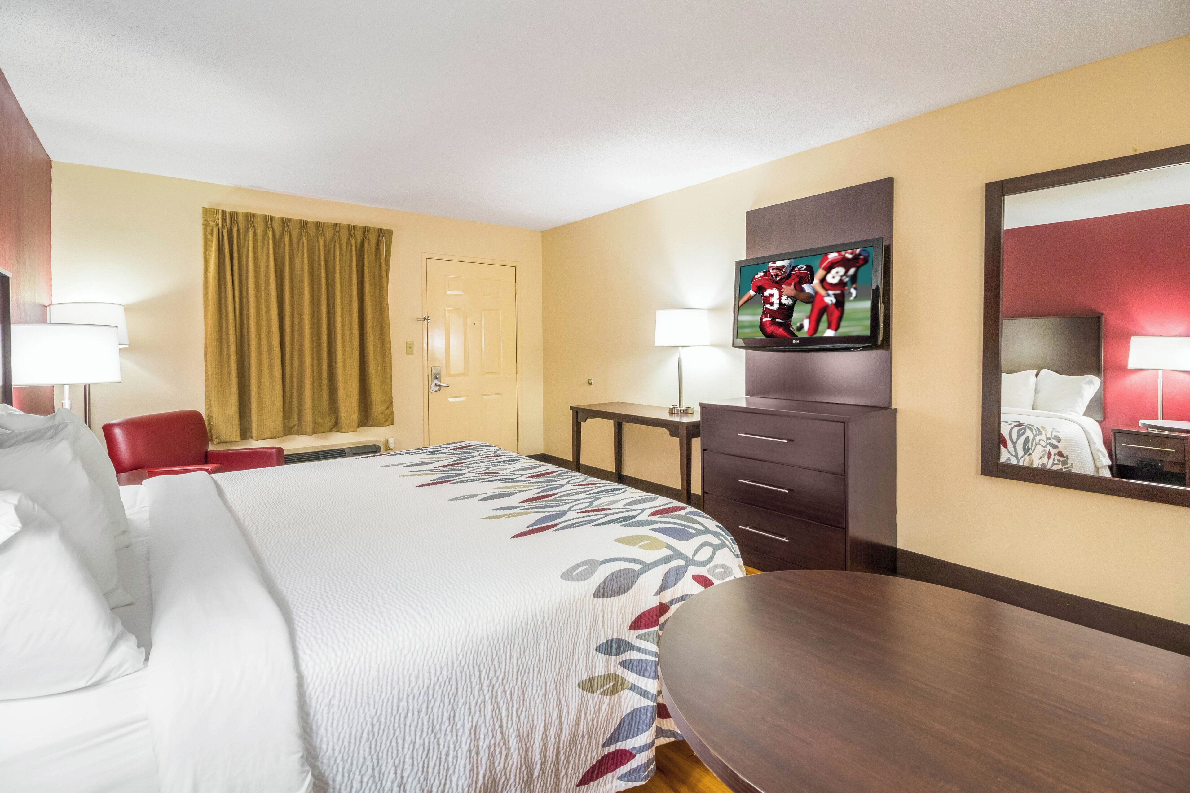 A hotel room with a bed, a desk, a television, and a mirror.