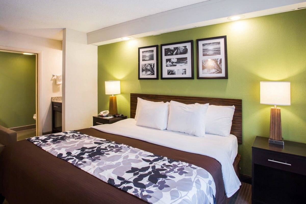 A hotel room with a bed, two bedside tables, a nightstand, a wall-mounted lamp, and three framed pictures on the wall.