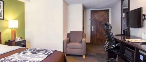 A hotel room with a bed, a desk with a chair, a TV, and a door leading to another room.