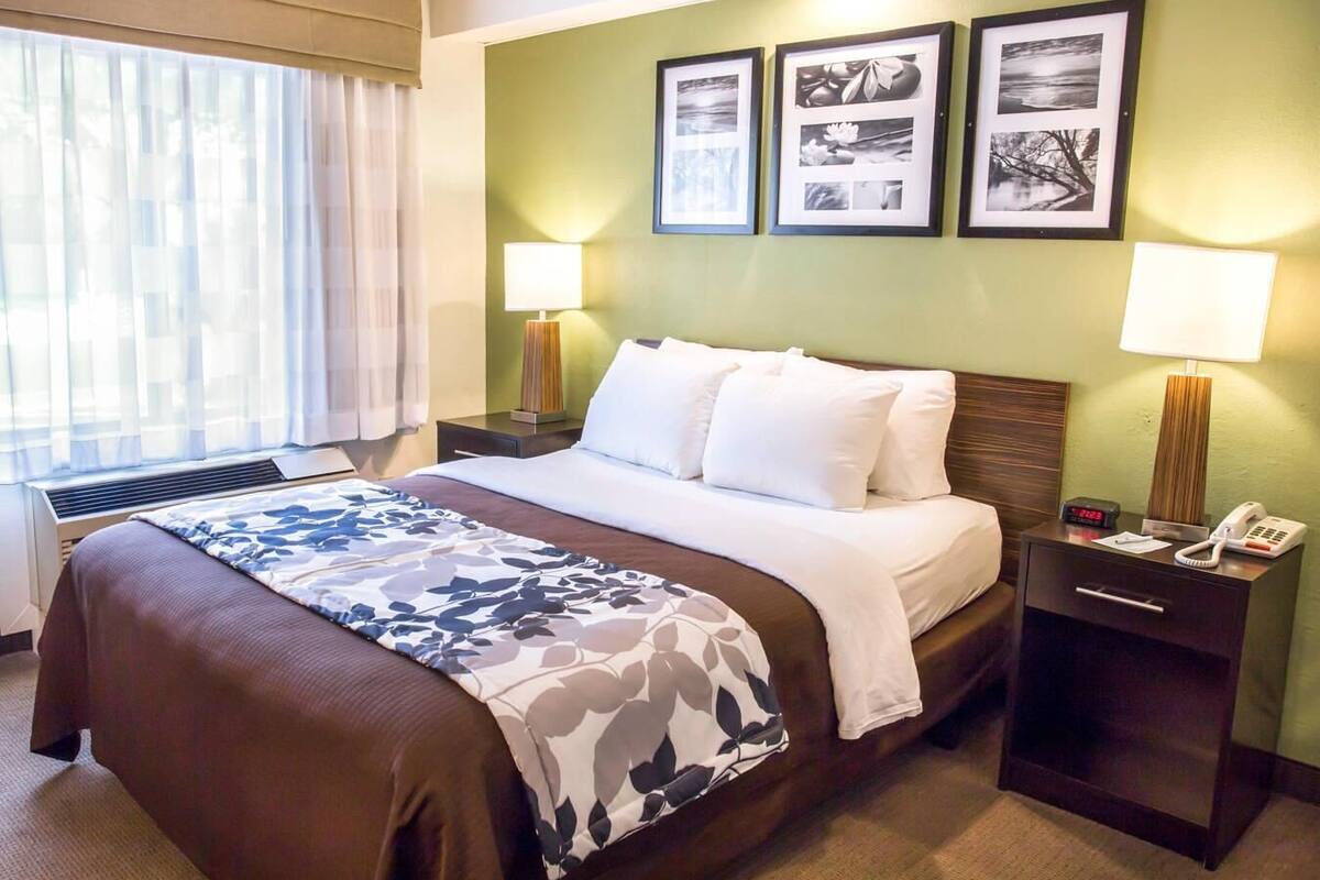 A hotel room with a large bed, two bedside tables, a desk with a lamp, and a window with curtains.