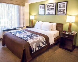 A hotel room with a large bed, two bedside tables, a desk with a lamp, and a window with curtains.