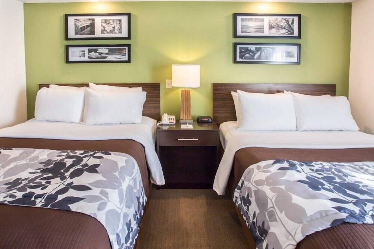 A hotel room with two beds, a nightstand, a lamp, and framed pictures on the wall.