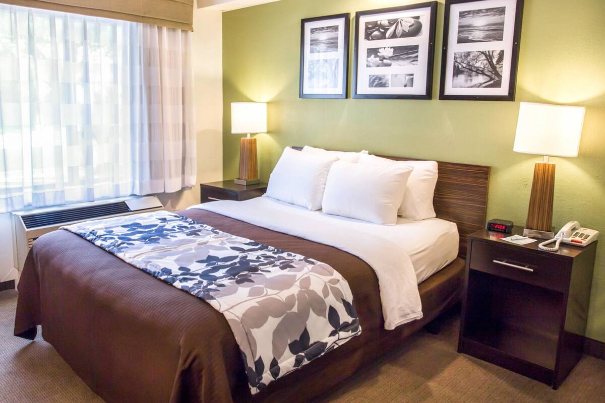 A hotel room with a bed, bedside lamps, a nightstand with a phone, and framed pictures on the wall.
