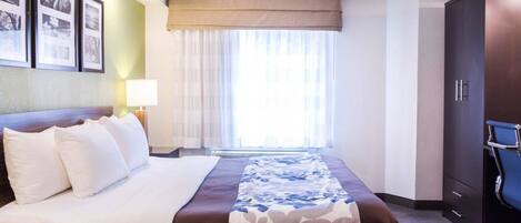 Una habitación de hotel con una cama grande, un escritorio, una silla, un armario y una ventana con cortinas.