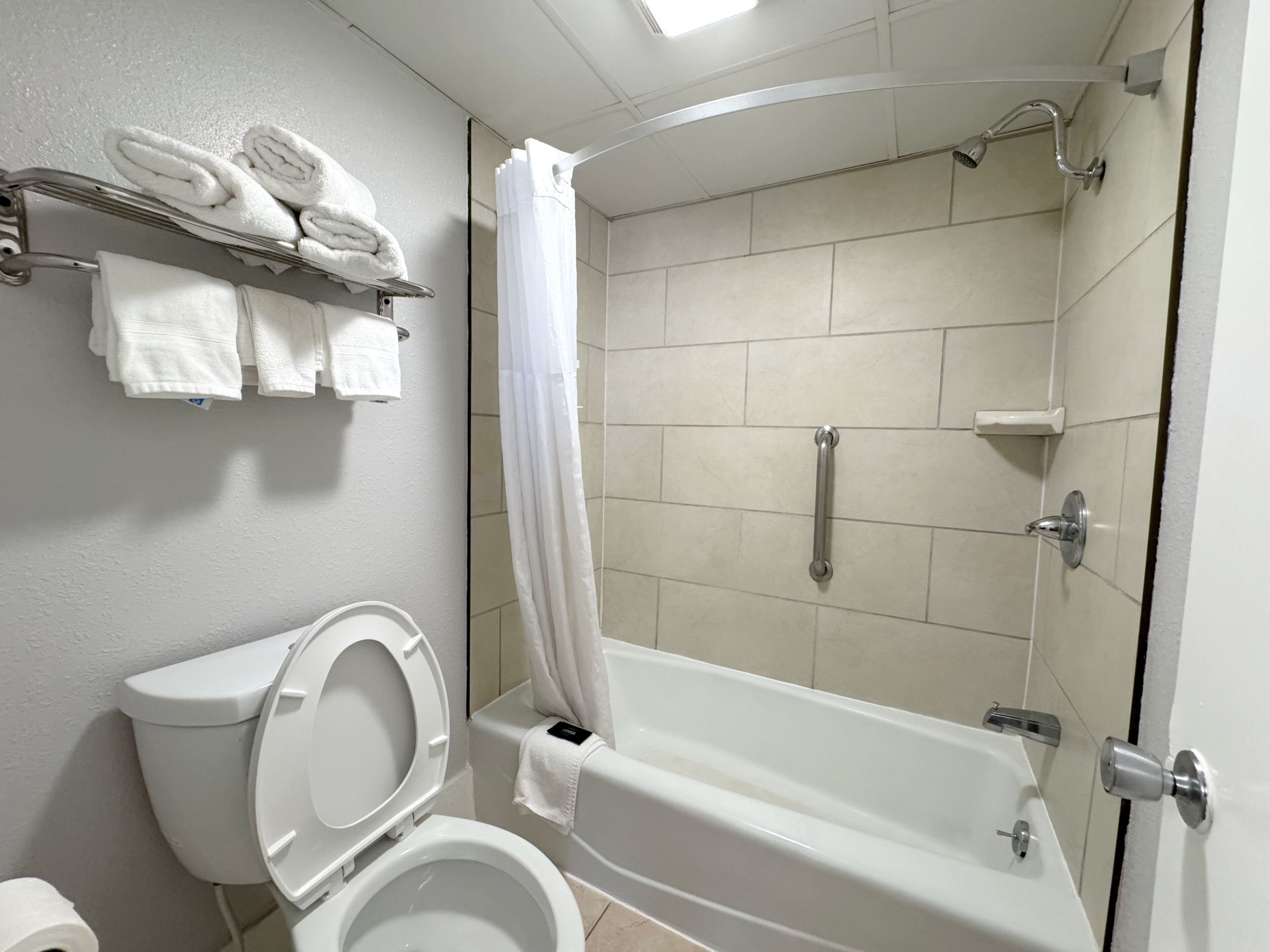 Un baño con inodoro, bañera, ducha y un perchero con toallas dobladas.