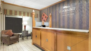 Un espace d’accueil comprenant un comptoir de réception en bois, une chaise, une lampe et un mur sur lequel est inscrit le nom « Baymont Inn & Suites ».
