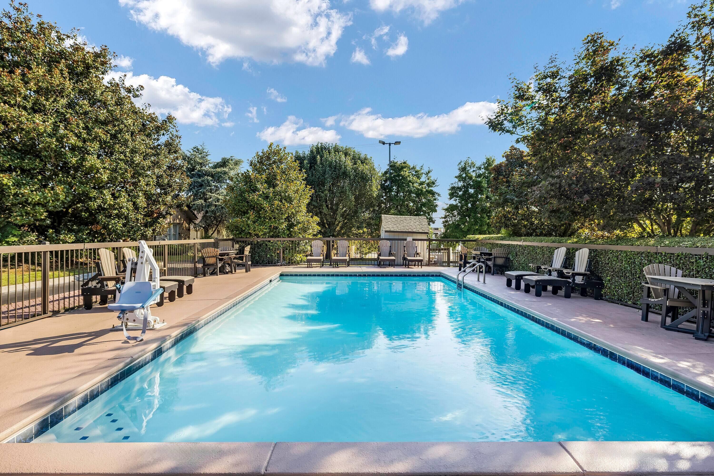 A rectangular swimming pool with a tiled edge, surrounded by a deck area with chairs and tables.