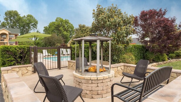 Une terrasse extérieure dotée d’un foyer, de sièges en pierre et d’une piscine en arrière-plan.