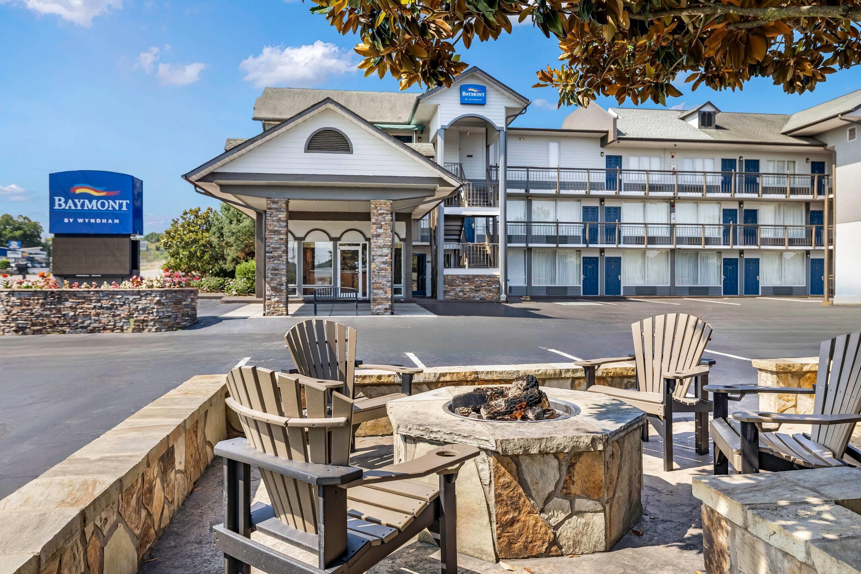 A hotel entrance with a covered outdoor seating area, a fire pit, and a sign for the Baymont by Wyndham hotel.