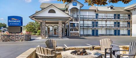 A hotel entrance with a covered outdoor seating area, a fire pit, and a sign for the Baymont by Wyndham hotel.
