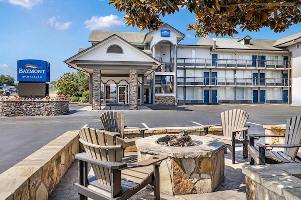 A hotel entrance with a covered outdoor seating area, a fire pit, and a sign for the Baymont by Wyndham hotel.