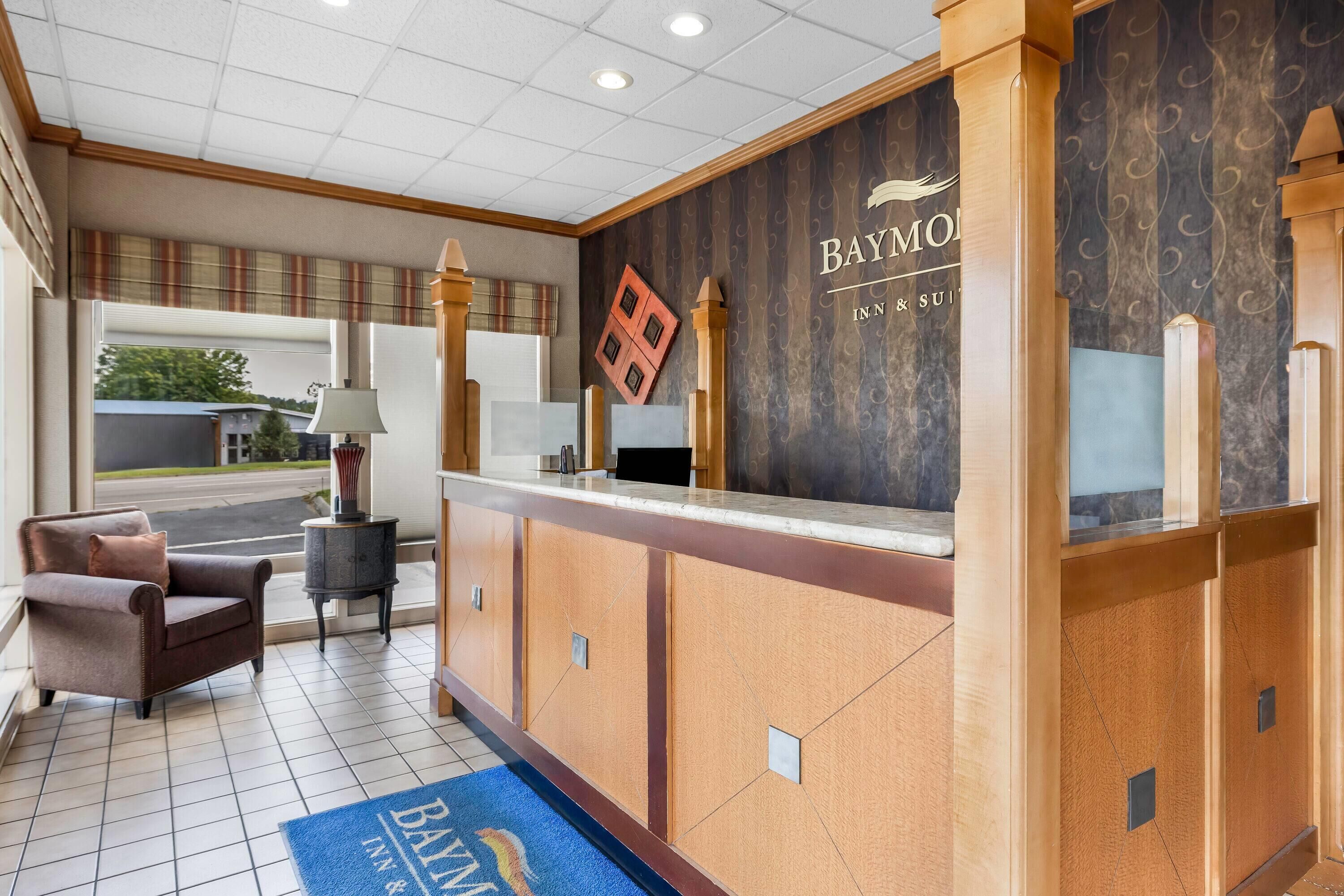 Un espace d’accueil d’hôtel comprenant un comptoir de réception, un espace d’attente avec un canapé et des fauteuils, et une vue sur l’extérieur.
