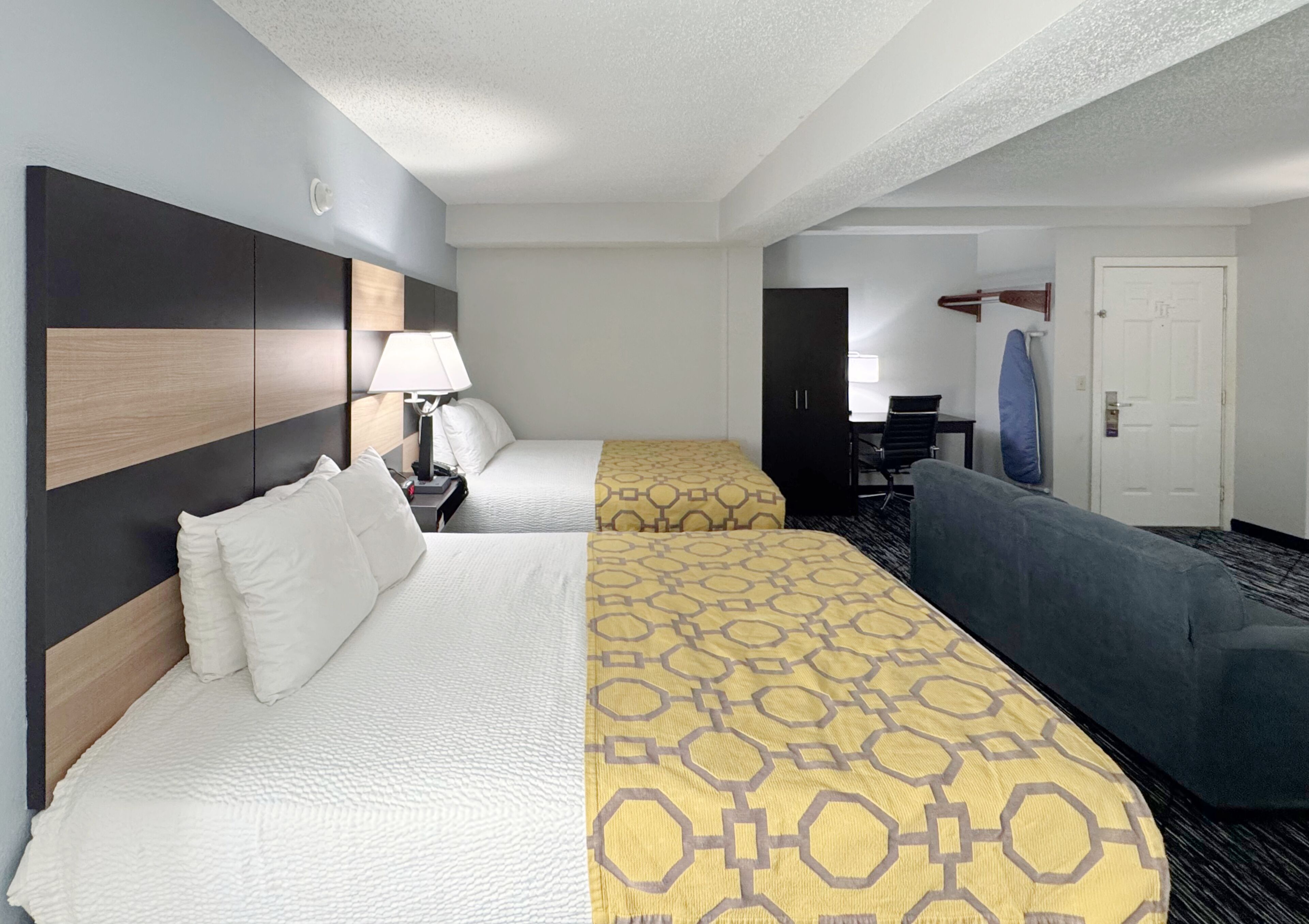 A hotel room with two beds, a desk, a chair, and a door.