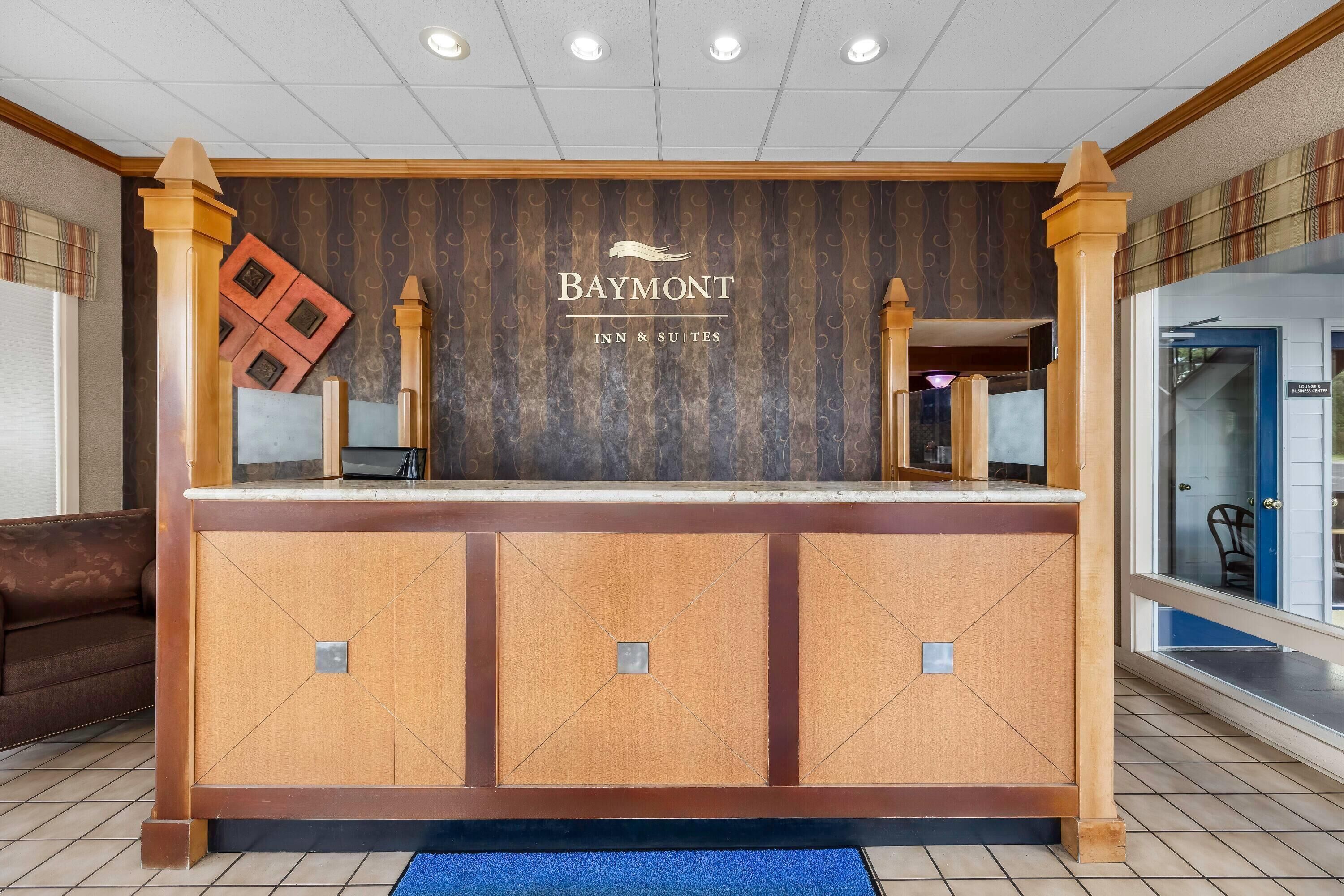 A reception desk with a wooden finish, a sign reading 'Baymont Inn & Suites,' and a blue carpet leading to the entrance.