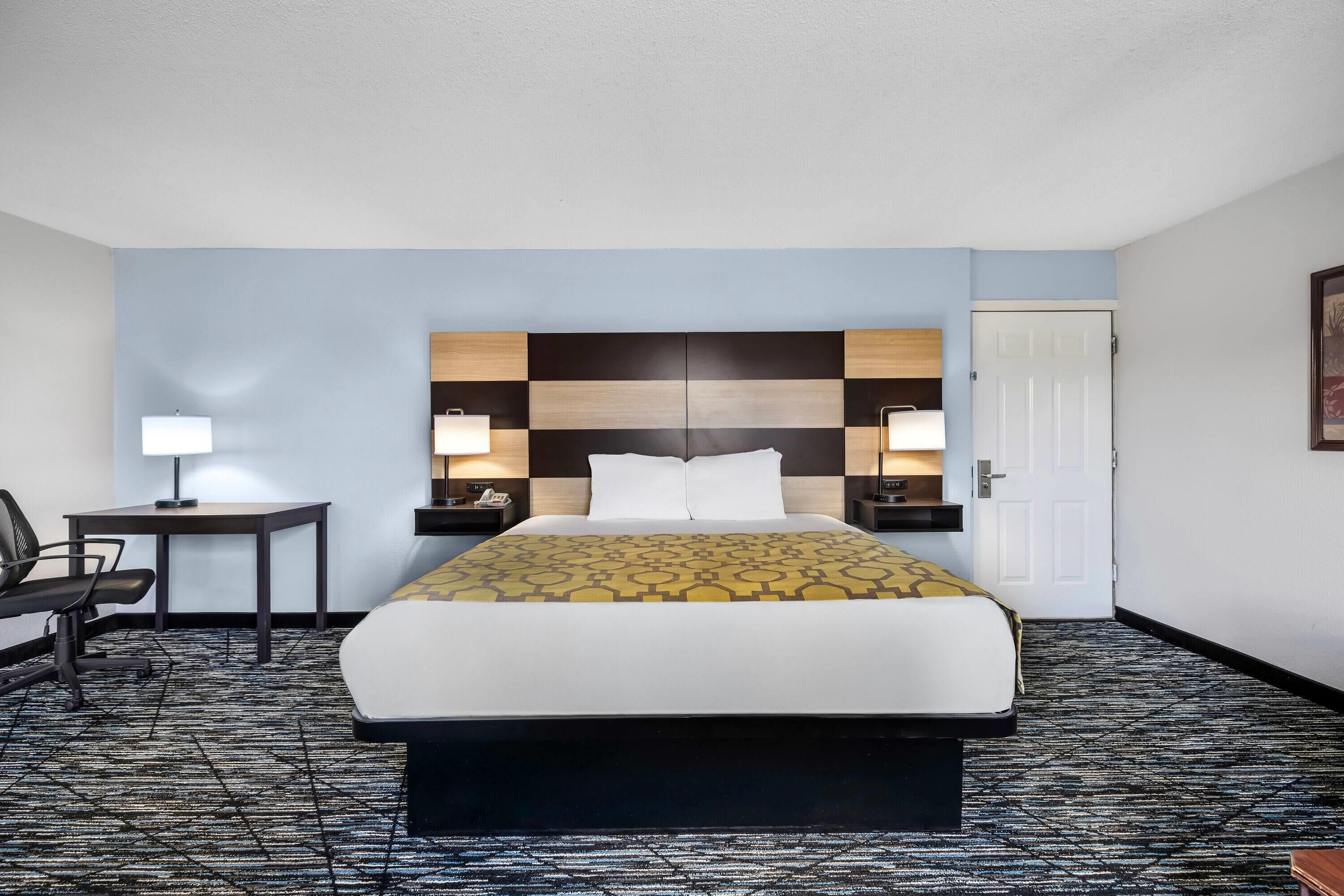Una habitación de hotel con una cama grande, mesitas de noche con lámparas, un escritorio y una silla.