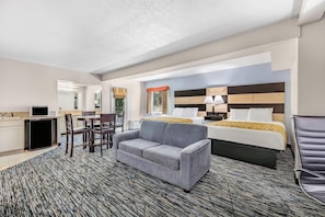 A hotel room with a bed, a sofa, a desk with a computer, and a chair.