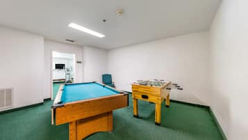 A room with a pool table, a foosball table, and a chair.