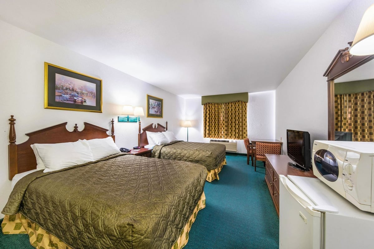 A hotel room with two beds, a desk, a television, and a microwave.