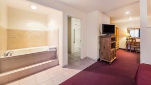 Quarto de hotel com uma banheira grande, televisão sobre um móvel de madeira e uma mesa de trabalho com uma cadeira.