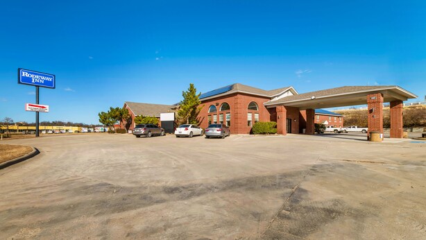 A motel with a clear sign, a parking lot, and a gas station. - Travelodge by Wyndham Decatur TX I-287 (Decatur)
