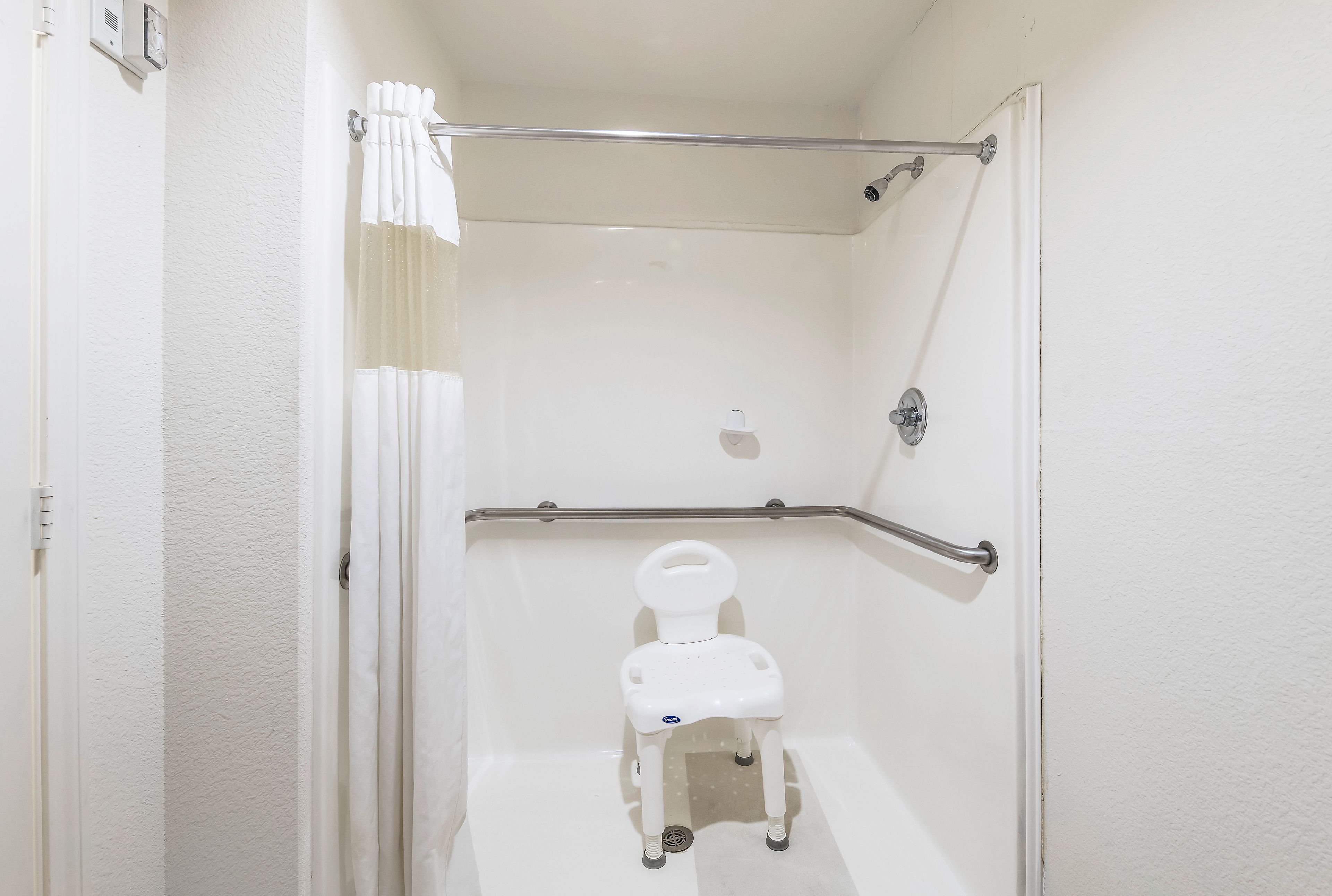 Un cuarto de baño accesible para sillas de ruedas, con inodoro blanco, barras de apoyo y ducha.