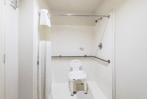 Un cuarto de baño accesible para sillas de ruedas, con inodoro blanco, barras de apoyo y ducha.