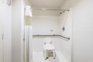 Un cuarto de baño accesible para sillas de ruedas, con inodoro blanco, barras de apoyo y ducha.