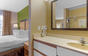 Una habitación de hotel con cama, baño con lavamanos, espejo y toallero.