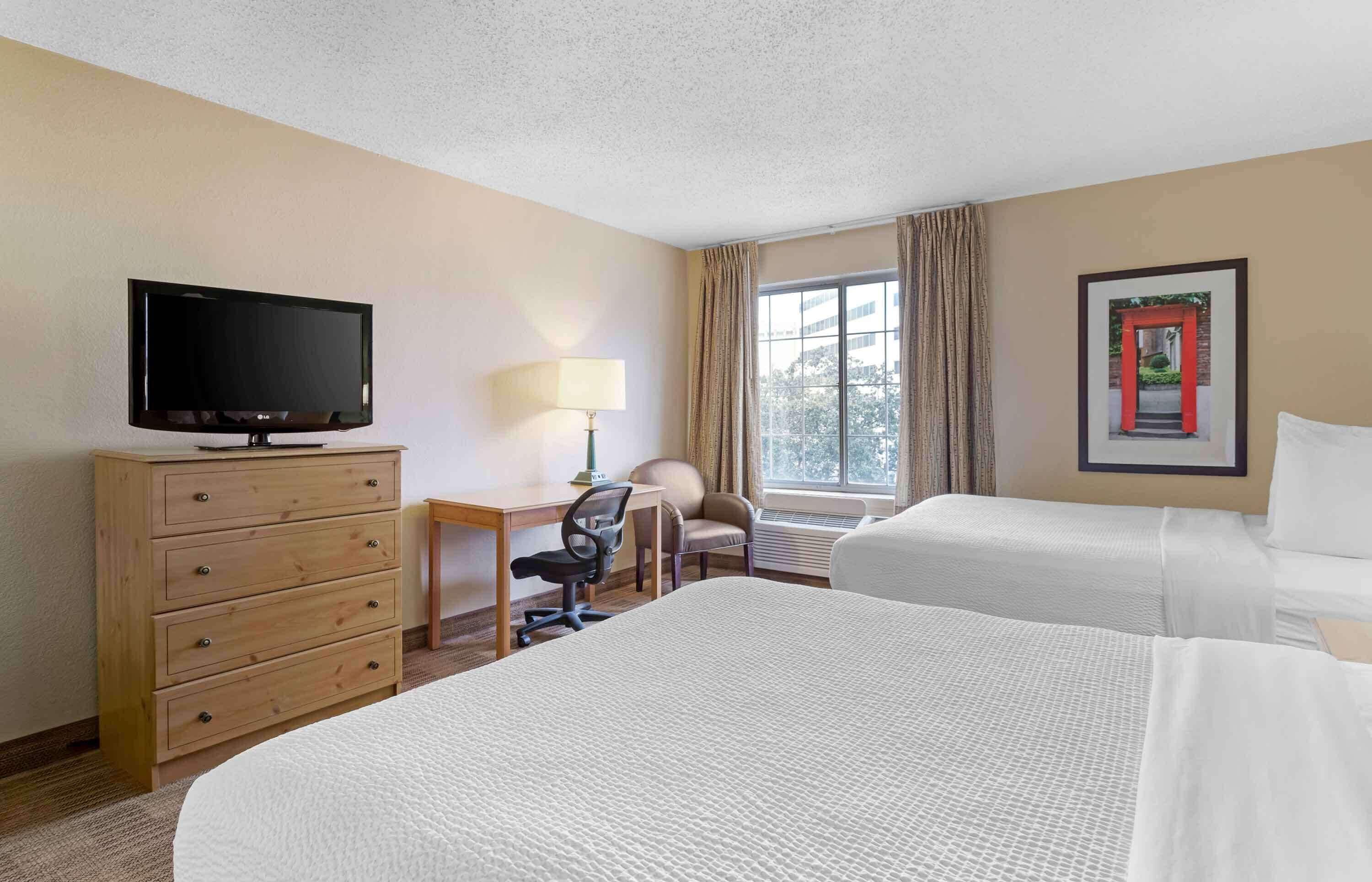 A hotel room with two beds, a desk with a chair, a television, and a window with curtains.