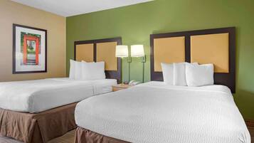 A hotel room with two beds, each with a headboard, white bedding, and a bedside table with a lamp.