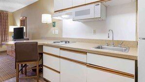 A compact hotel kitchen with a microwave, sink, and a small dining area with a chair and table.