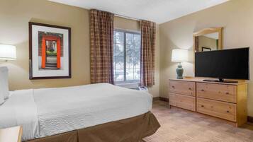 Una habitación de hotel con cama, televisión, cómoda y ventana con cortinas.