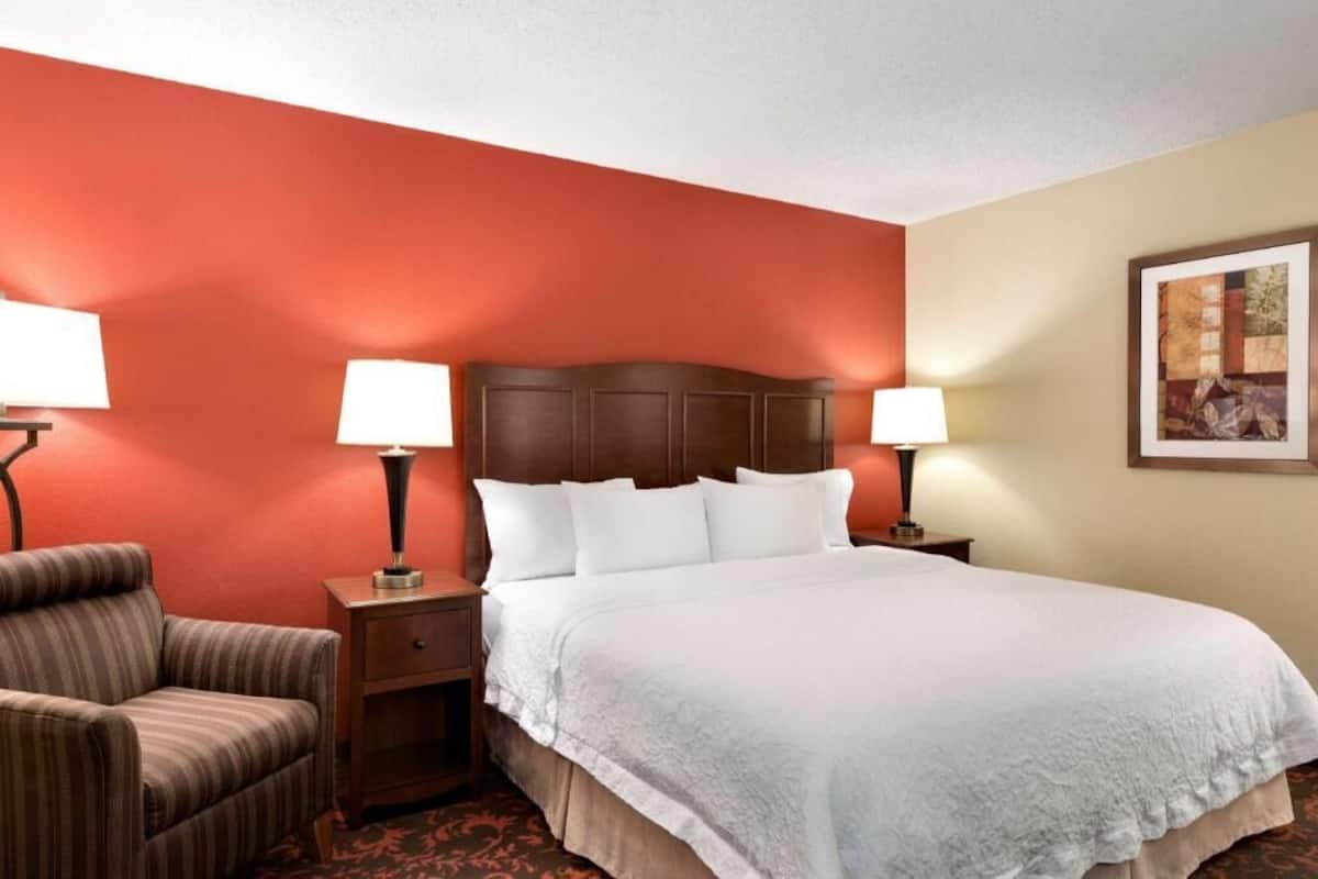 A hotel room with a large bed, two bedside lamps, a chair, a nightstand, and a framed picture on the wall.