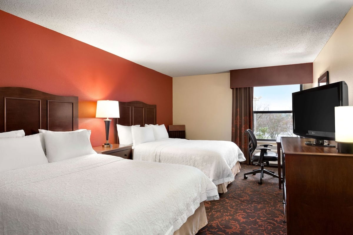 A hotel room with two beds, a desk, a television, and a window.