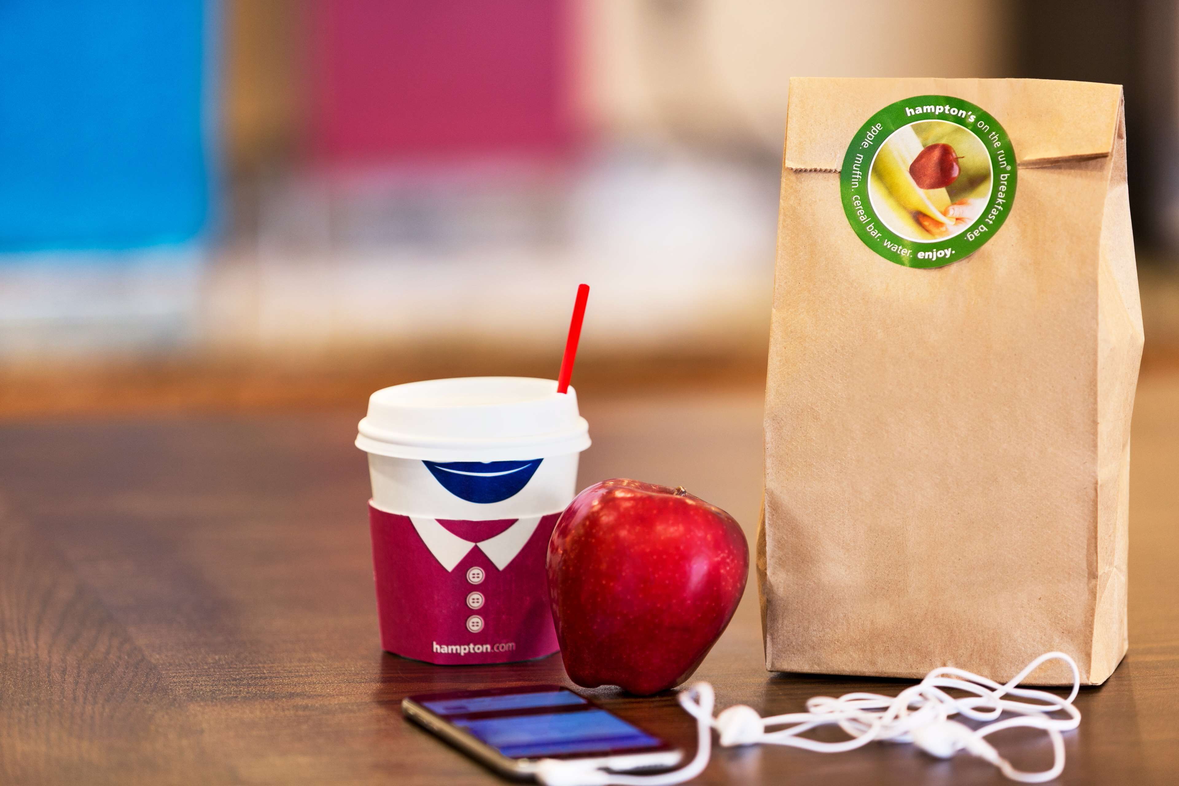 Una taza de café, una bolsa de papel y una manzana sobre una mesa de madera.