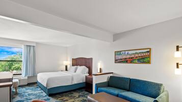 A hotel room with a bed, a sofa, a desk, and a window with a view of greenery.
