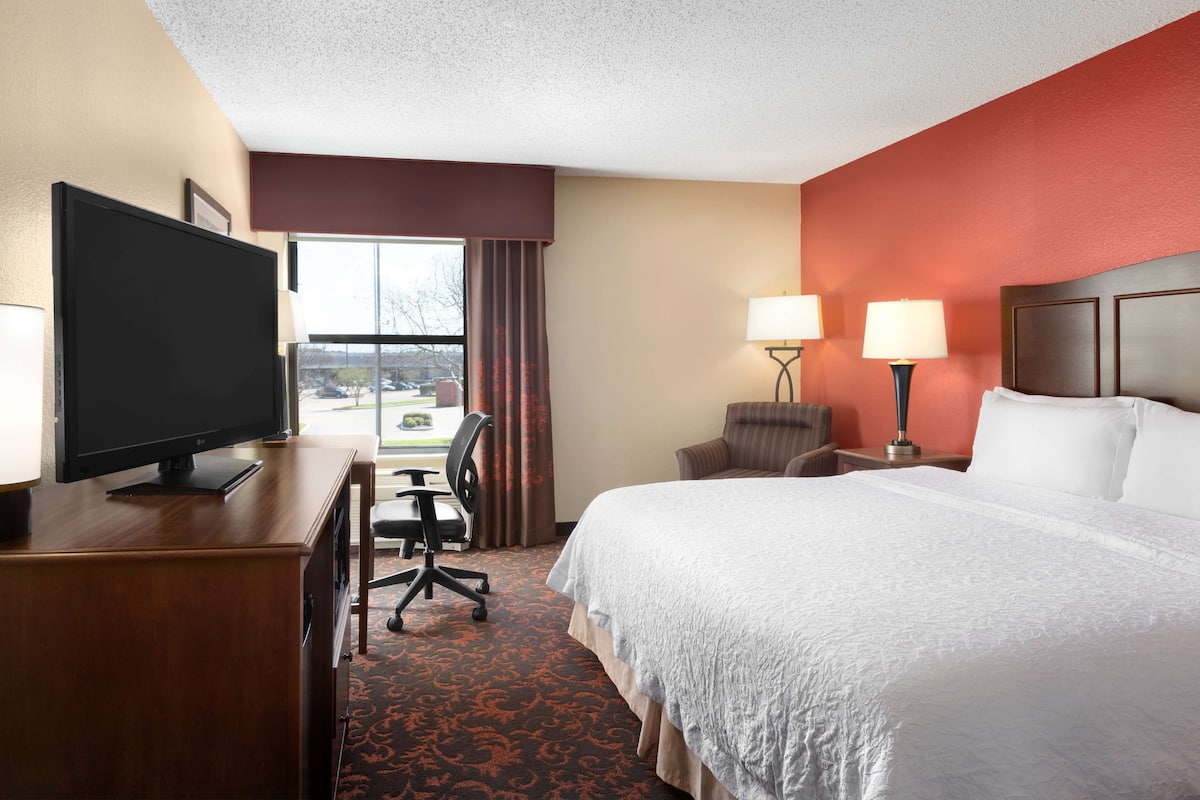 A hotel room with a bed, desk, television, and two lamps.