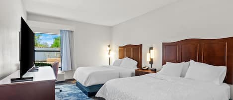 Habitación de hotel con dos camas, un escritorio, un televisor y una ventana con cortinas.
