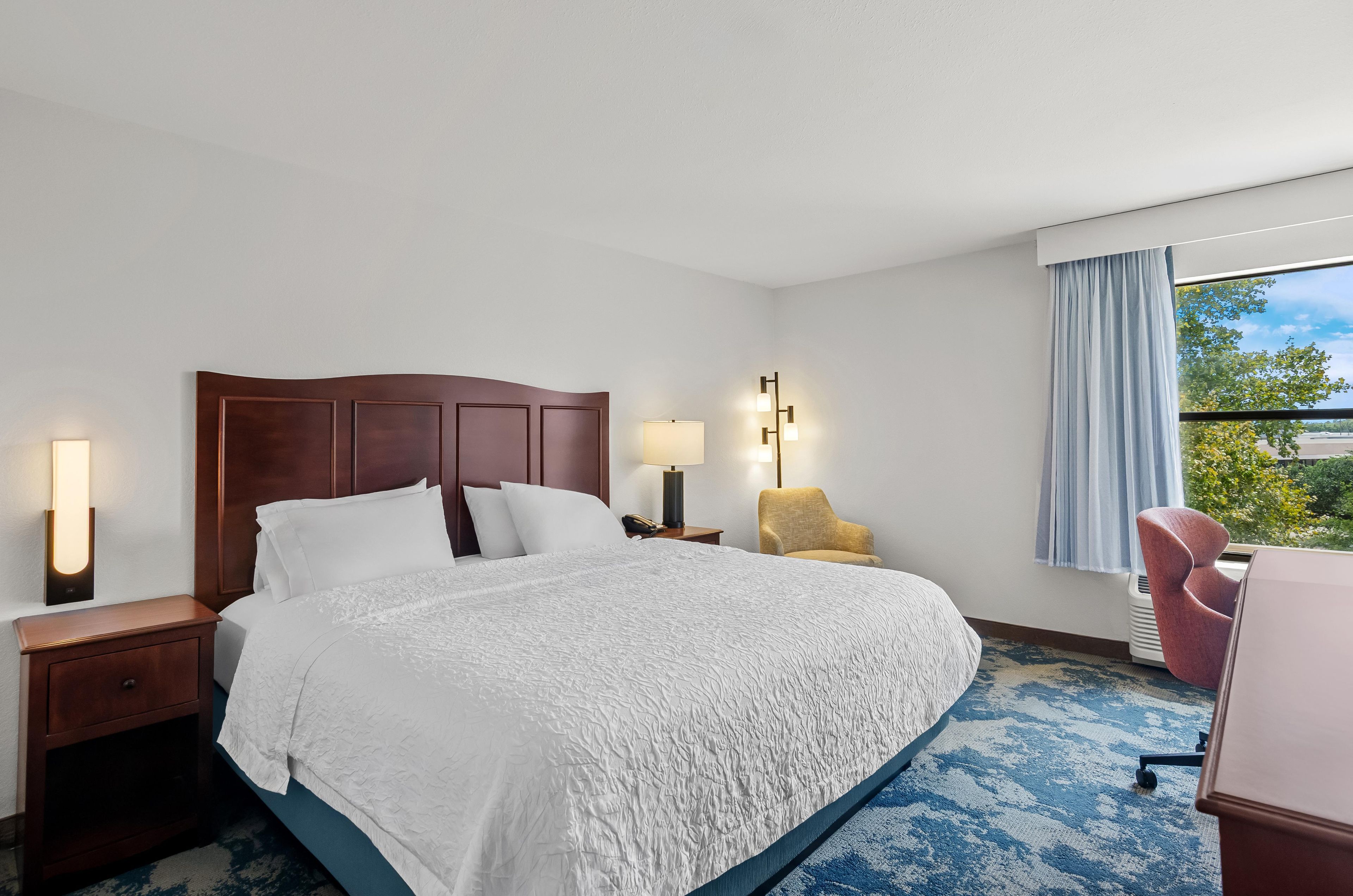 A hotel room with a large bed, bedside lamps, a chair, and a view of the outdoors.