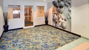 Um hall de hotel com carpete estampado, porta de entrada de vidro e um mural na parede.