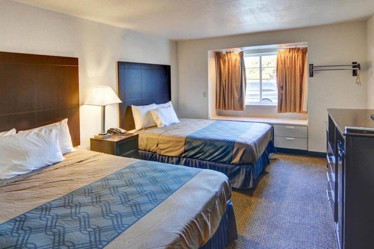 A hotel room with two beds, a desk, a lamp, a window with curtains, and a minibar.