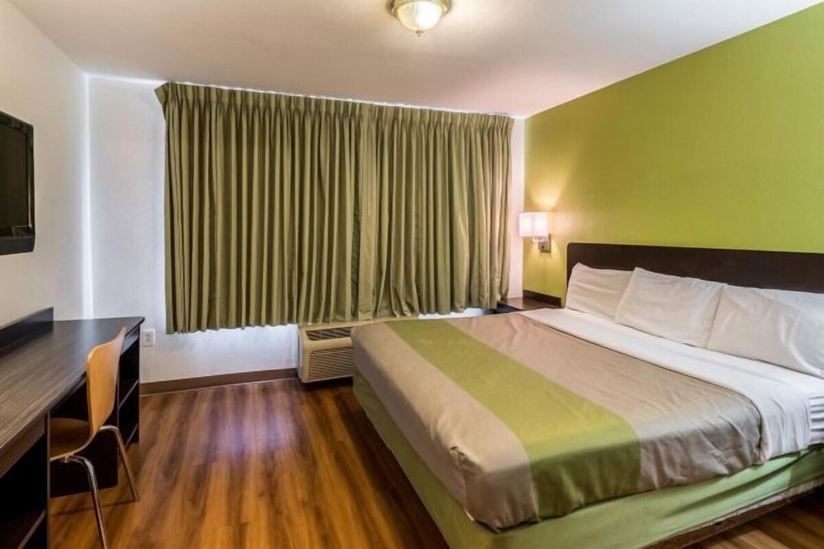 Een hotelkamer met een bed, een bureau, een stoel, een raam met gordijnen en een wandlamp.