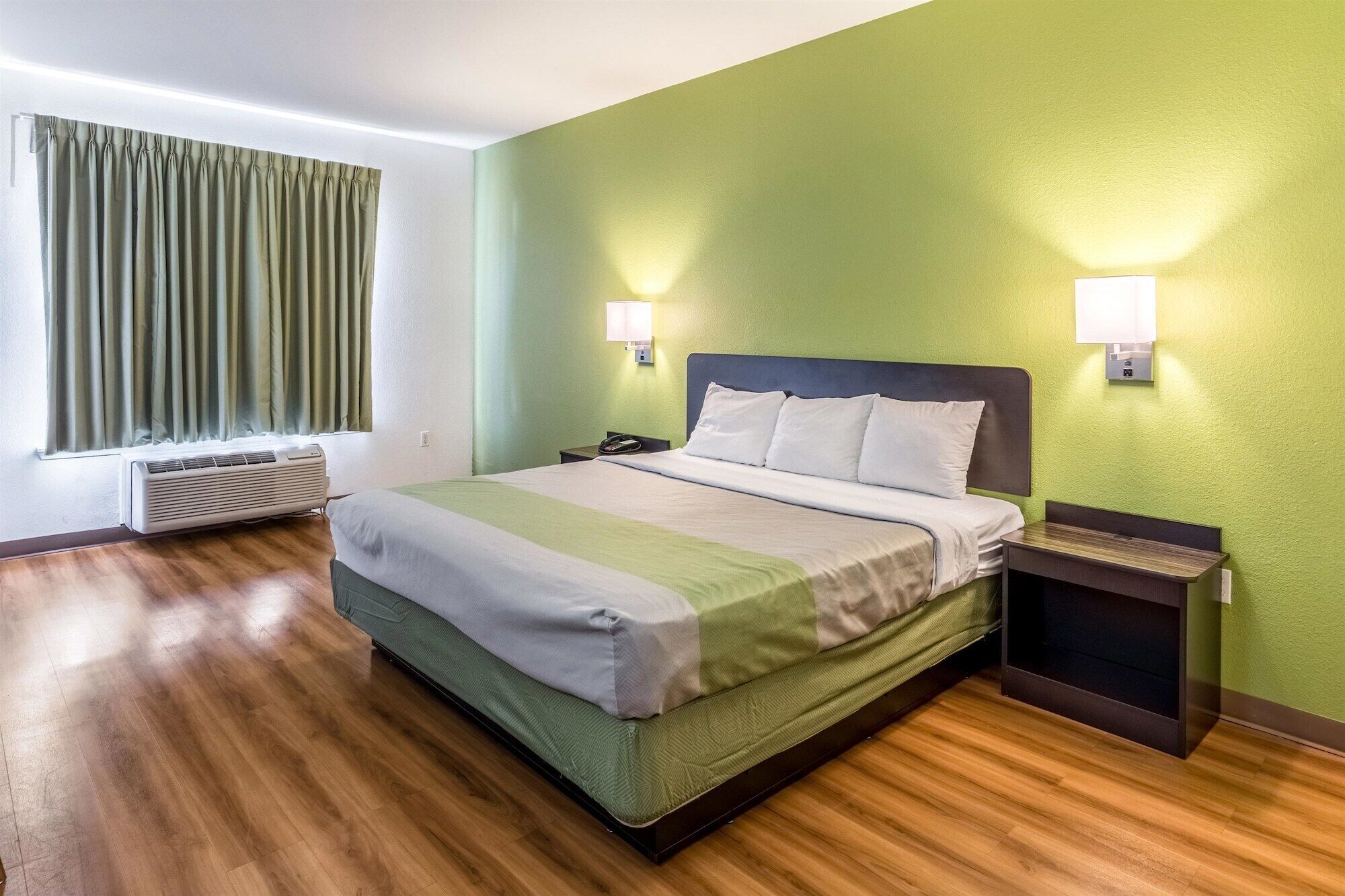 Una habitación de hotel con una cama, una mesita de noche, una lámpara y una ventana con cortinas.