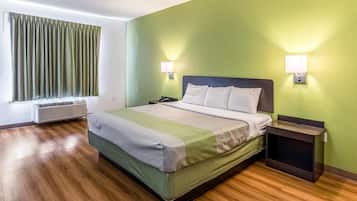 Una habitación de hotel con una cama, una mesita de noche, una lámpara y una ventana con cortinas.