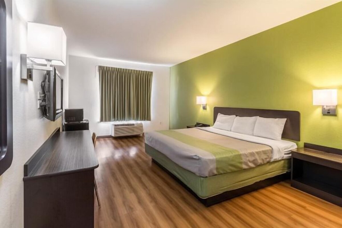 A hotel room with a bed, bedside table, lamp, and a window with curtains.